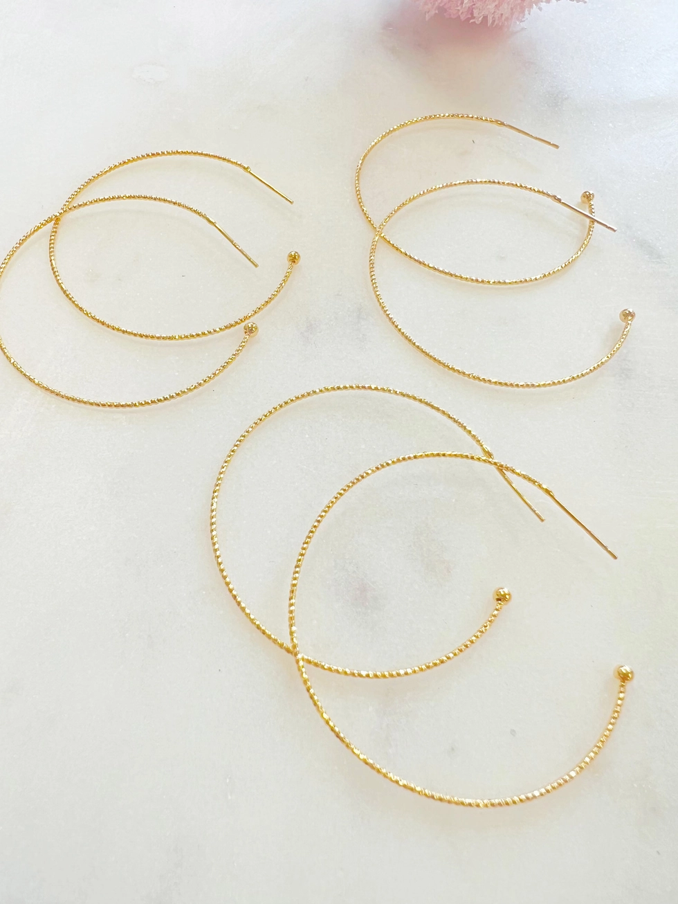 Three pairs of textured gold-plated hoops shown for styling; sold as one pair