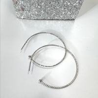 Close-up of slender textured silver-tone hoop earrings