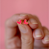 Hot pink enamel heart studs with gold-tone borders held in hand